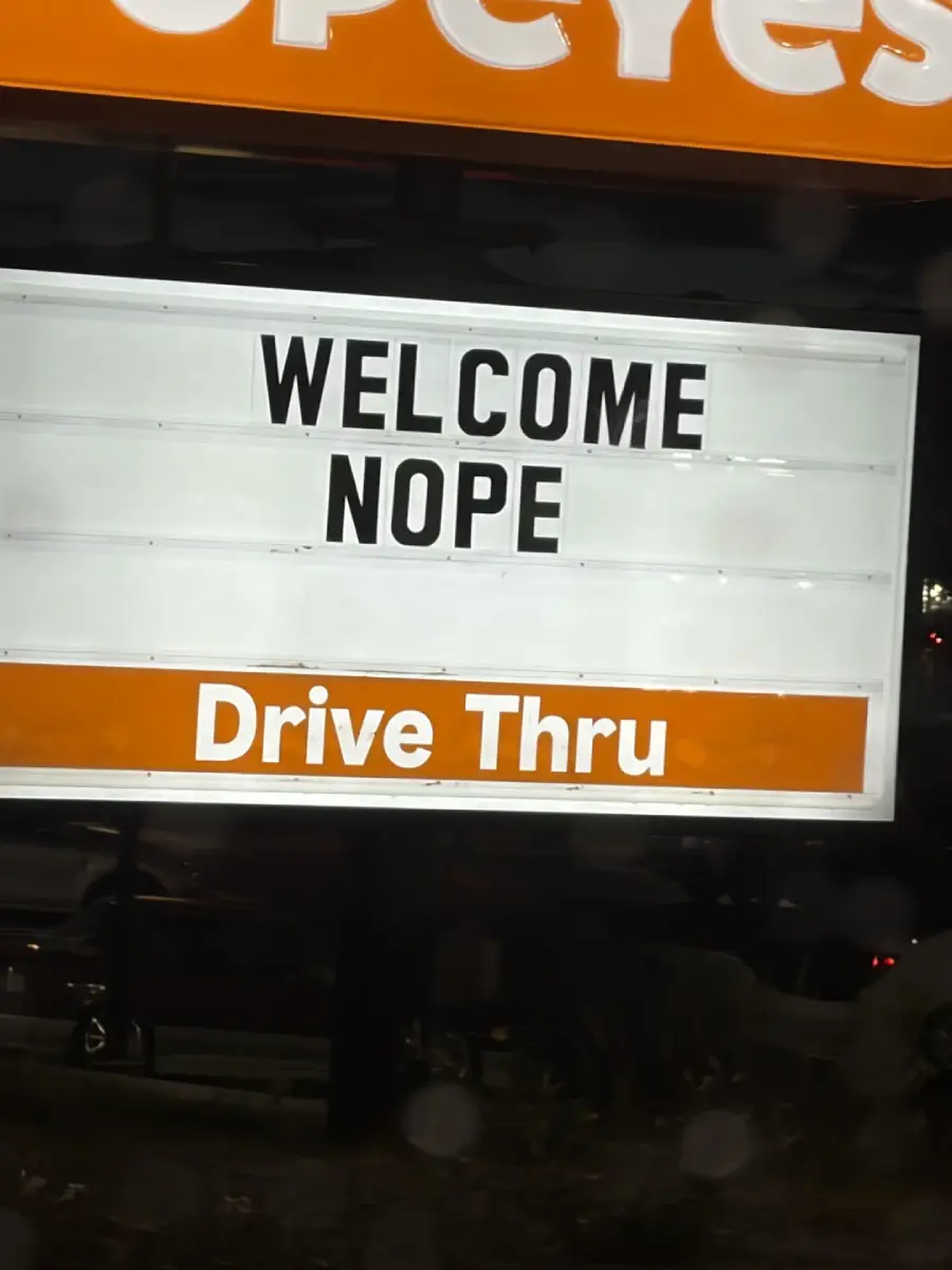 A Popeyes drive-thru sign reads “WELCOME NOPE” in black letters, with “Drive Thru” in an orange section below.
