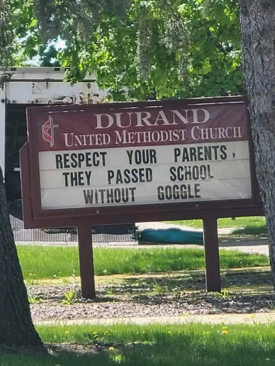 A church sign reads: “Respect your parents, they passed school without Google.” The sign is outdoors, surrounded by grass, trees, and a building in the background.