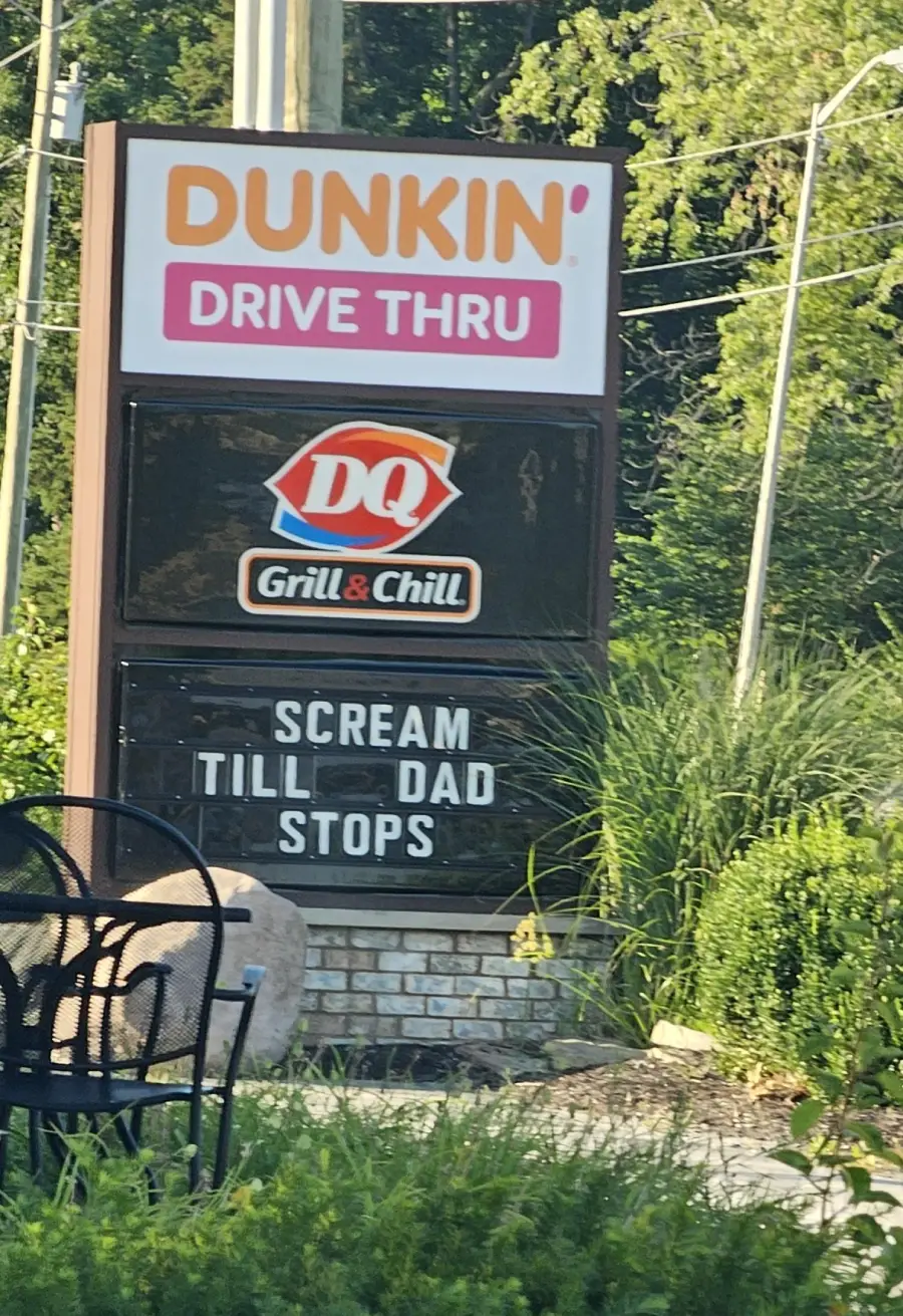 A sign for Dunkin’ and Dairy Queen Grill & Chill reads, “SCREAM TILL DAD STOPS,” with greenery and patio furniture nearby.