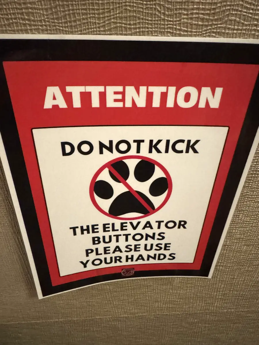 A sign reads, “Attention: Do not kick the elevator buttons, please use your hands,” with a graphic of a foot in a red circle with a slash through it.