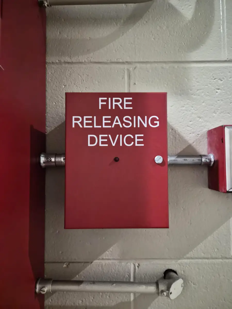 Red metal box mounted on a wall labeled “FIRE RELEASING DEVICE” in white text, with a small keyhole and a button or knob below the label.