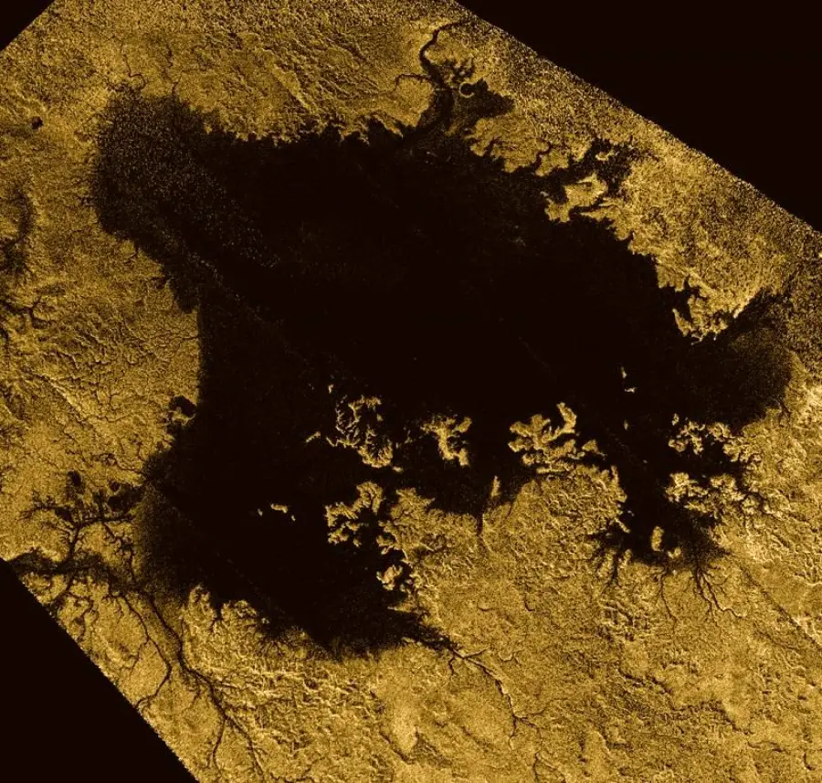A radar image shows a large, dark, irregularly shaped body of liquid surrounded by intricate, branching patterns on a textured golden surface, resembling a landscape seen from above.