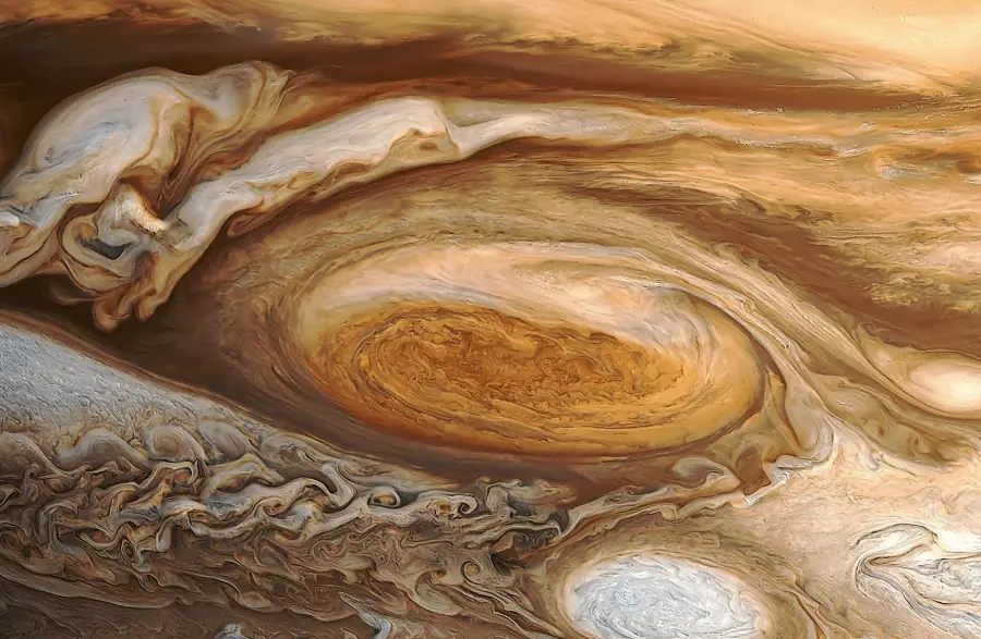 Close-up image of Jupiter’s swirling cloud patterns and the Great Red Spot, showing shades of brown, orange, white, and beige in a turbulent, vortex-like formation.