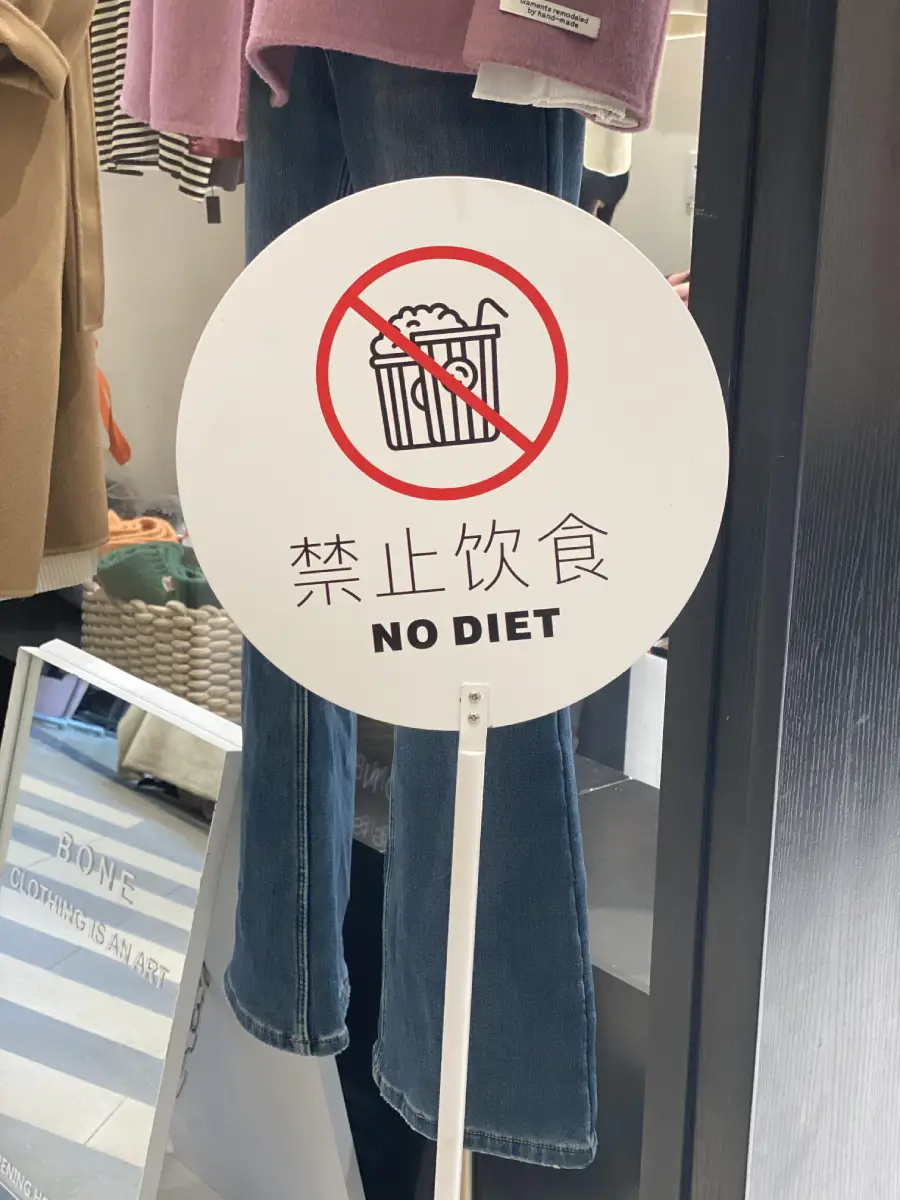 A round sign with a crossed-out image of fries and the words “NO DIET” and Chinese text below, displayed in front of clothing.