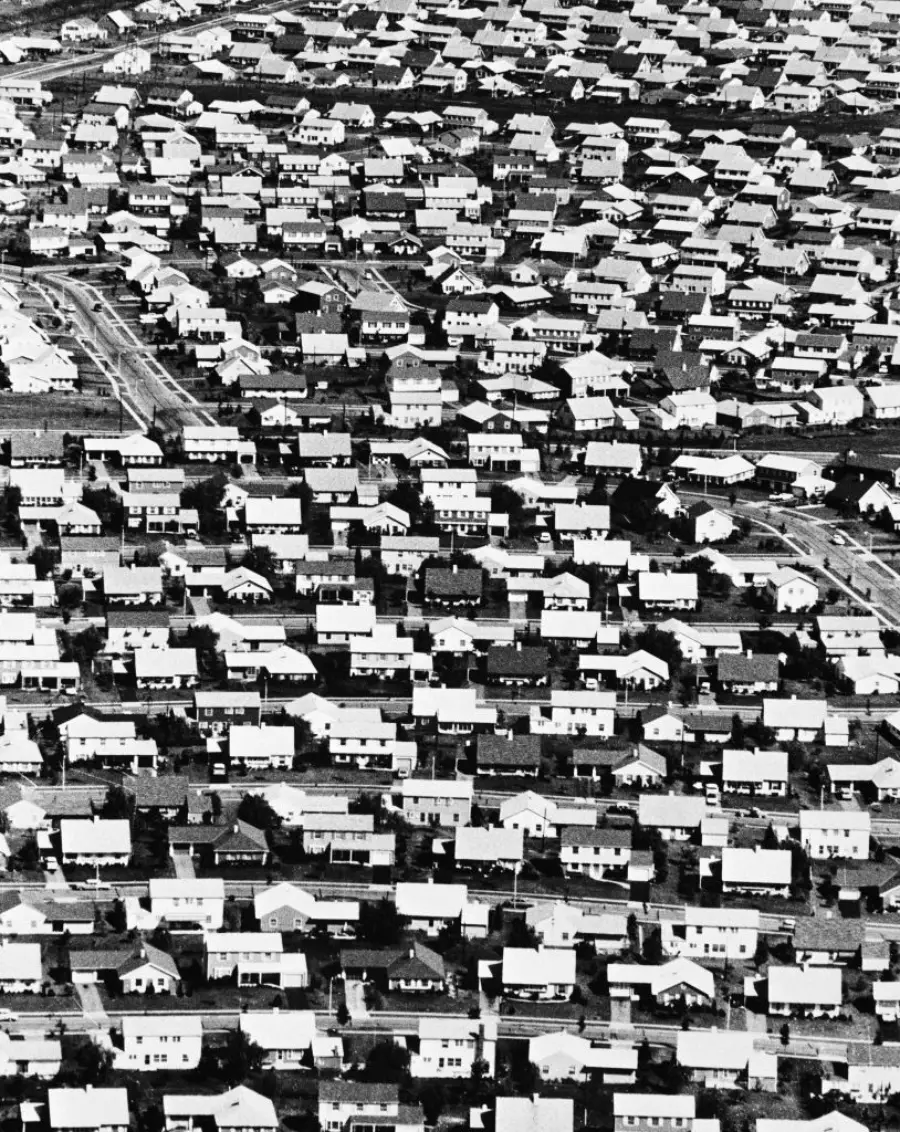 A black and white aerial photo shows a dense grid of nearly identical houses in a suburban neighborhood, illustrating a uniform postwar residential development.