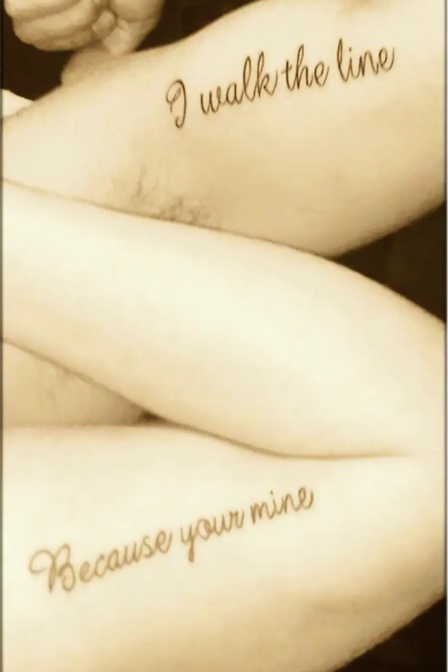 Two forearms with tattoos: one says “I walk the line” and the other says “Because your mine.” The image is sepia-toned.