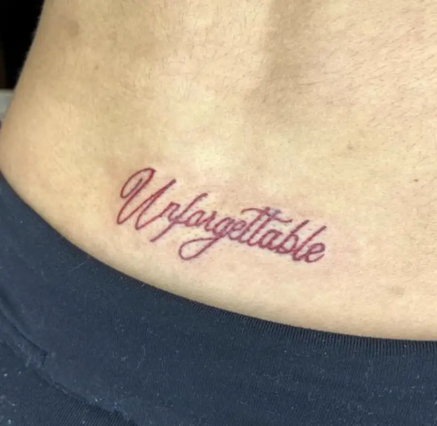 A tattoo on skin reads “Unforgattable” in cursive, with a spelling mistake. The person is wearing dark pants.