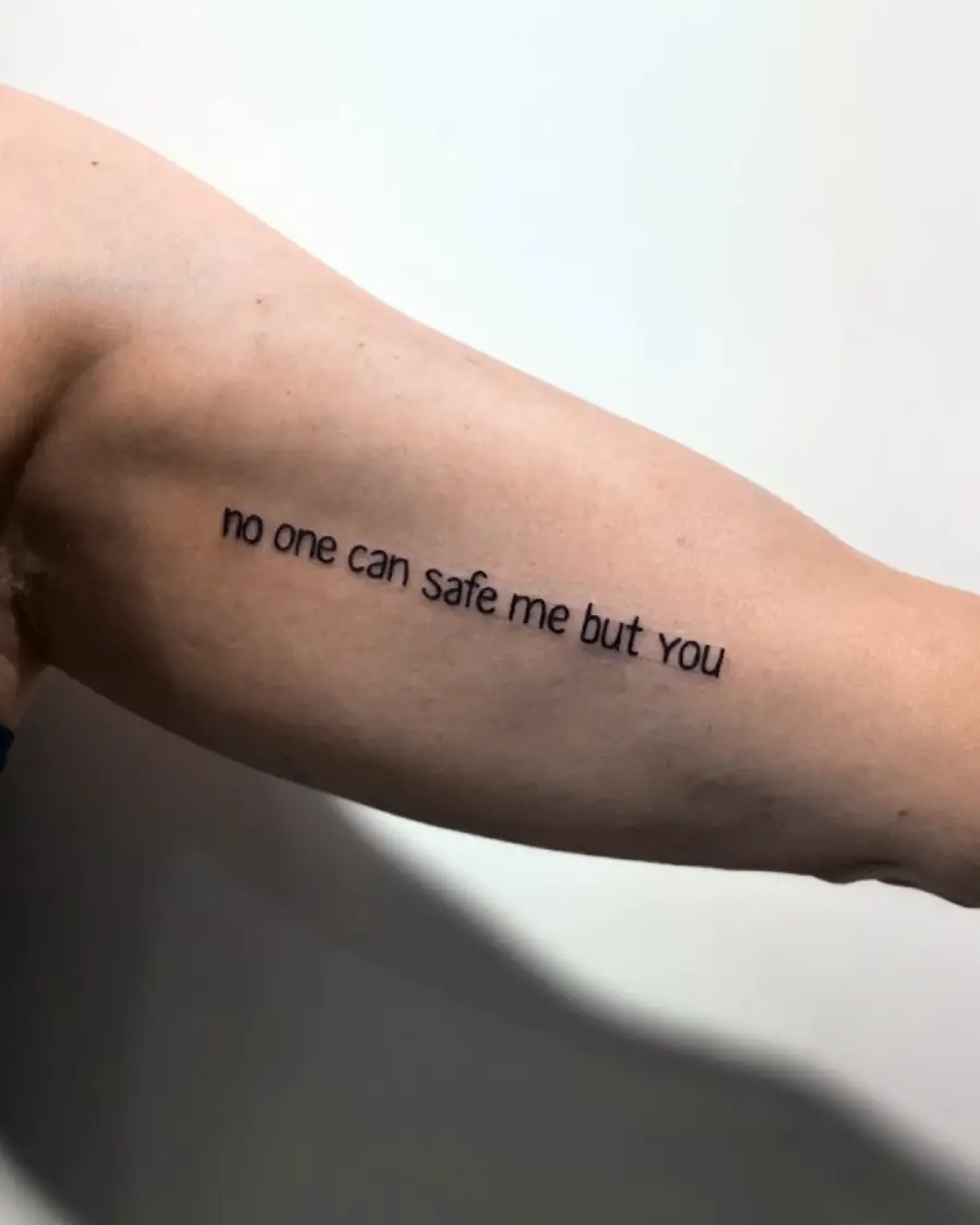 A tattoo on a person’s upper arm reads “no one can safe me but you” in black, lowercase letters on light skin.