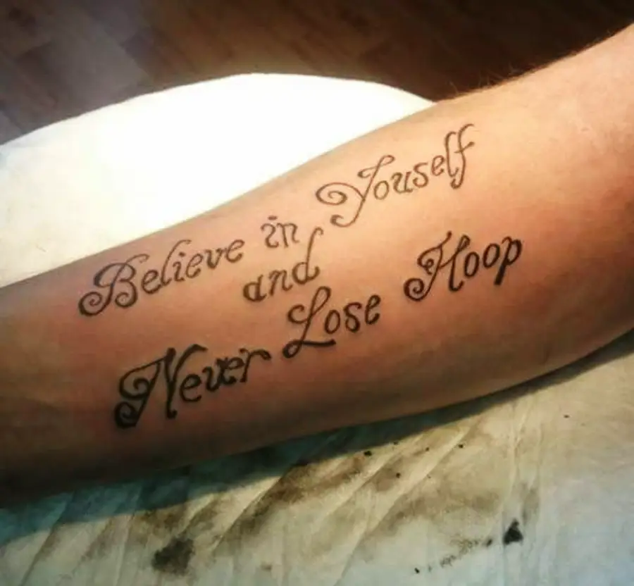 A tattoo on a forearm reads, “Believe in Yourself and Never Lose Hoop,” with “Hoop” appearing instead of “Hope.” The text is in decorative script.