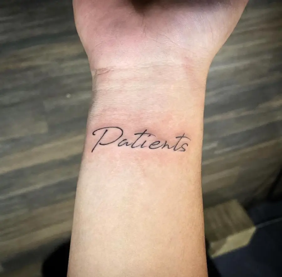 A wrist tattoo featuring the word “Patients” in a black, cursive font on light skin, with a blurred wooden floor background.