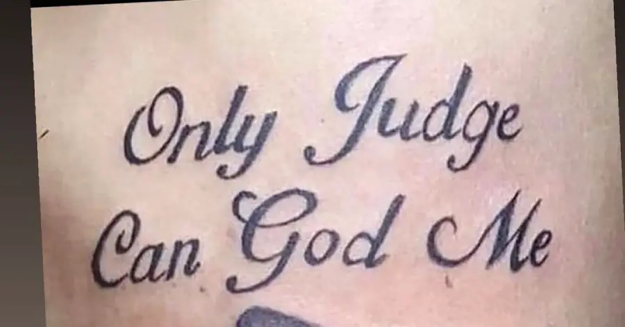 Tattoo with black cursive text that says “Only Judge Can God Me” on a person’s skin.