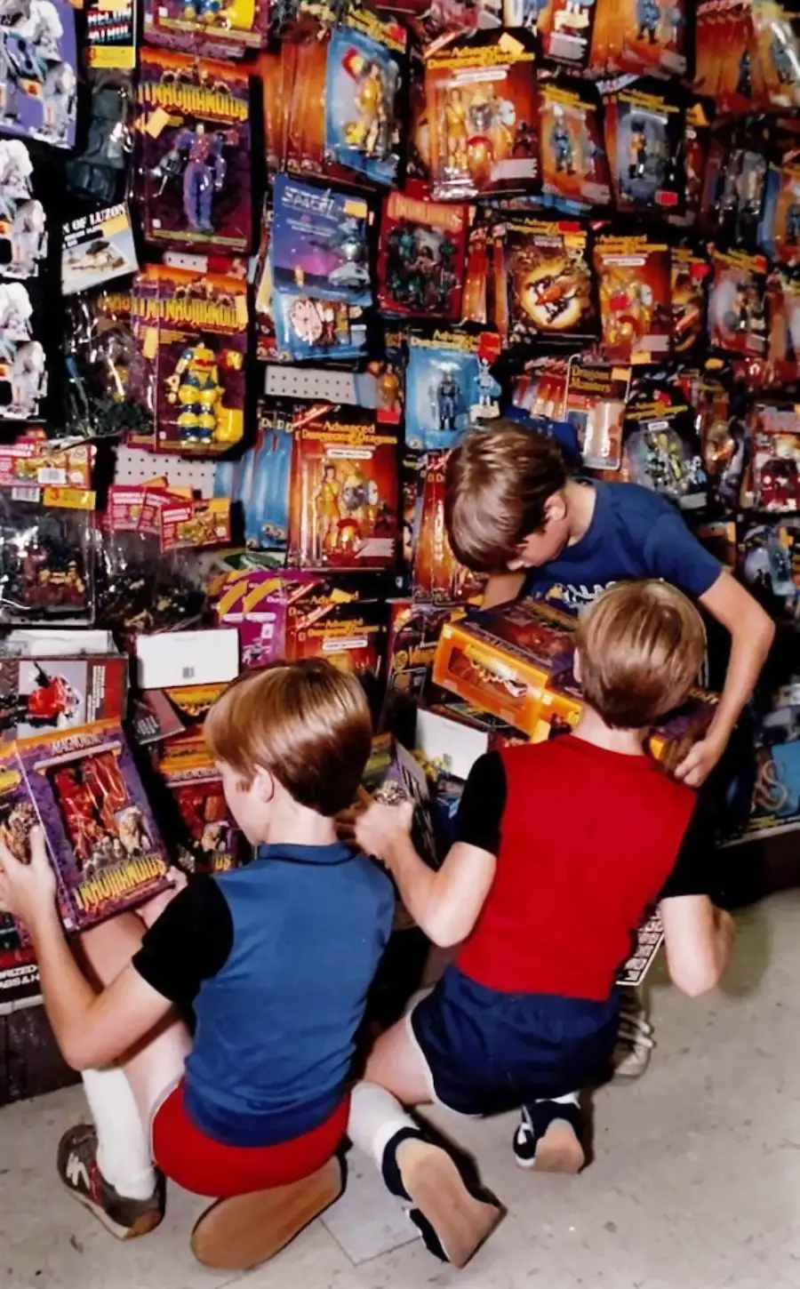 Three children look at action figures and toys on display in a store aisle, surrounded by shelves packed with colorful packaged toys.