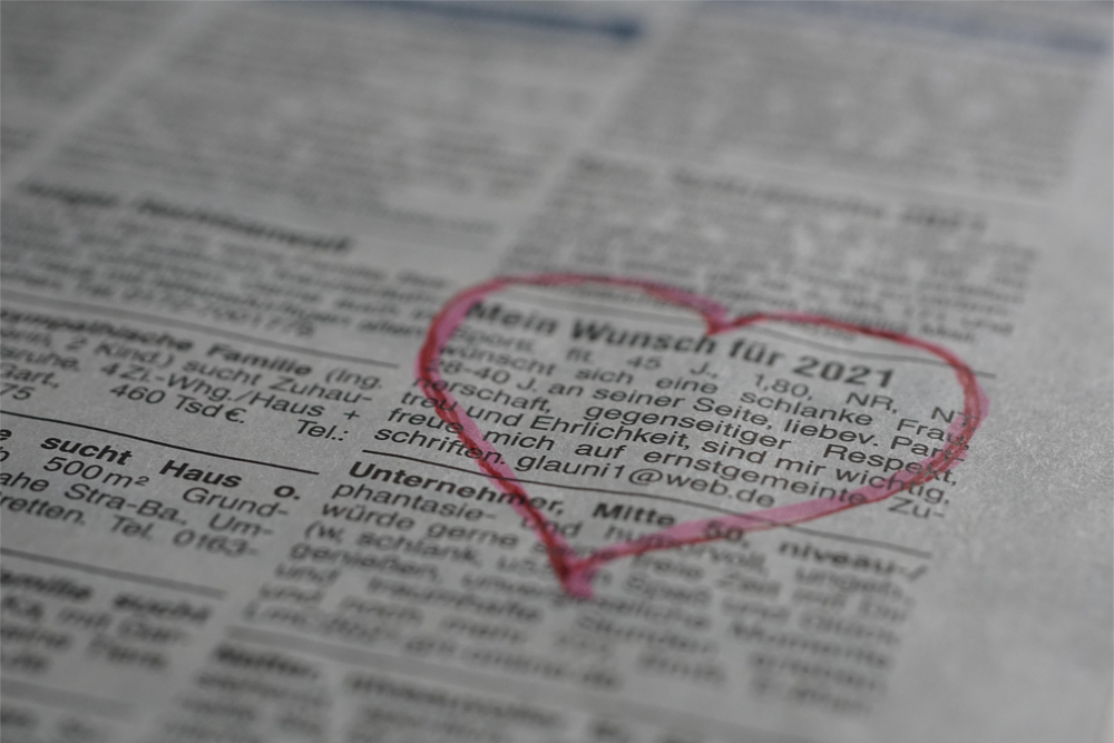 A newspaper classified ad in German is highlighted by a red heart drawn around it, indicating a personal or heartfelt message among the listings.