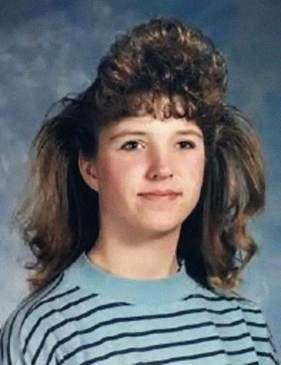 A young person with curly, voluminous hair and bangs wears a striped shirt and smiles slightly in a vintage-style portrait with a blue-gray background.