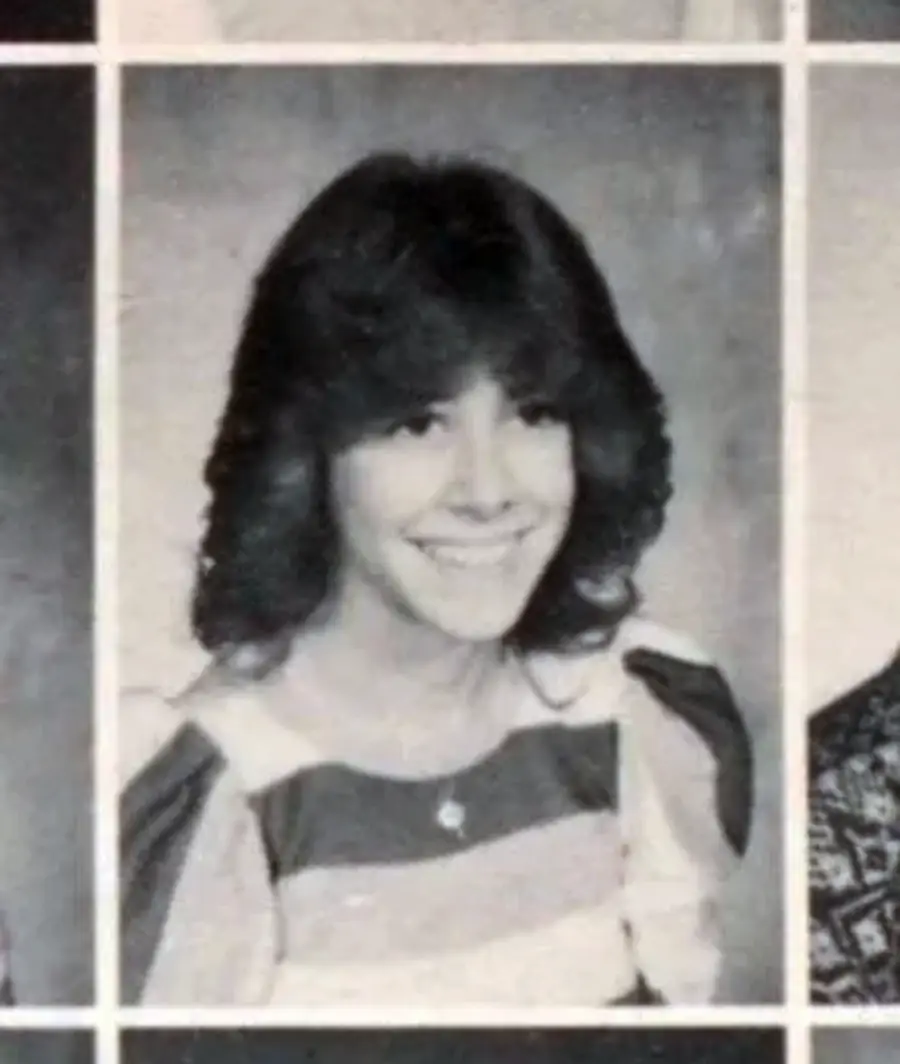 Black and white yearbook photo of a young person with shoulder-length dark hair, wearing a striped top and smiling at the camera.
