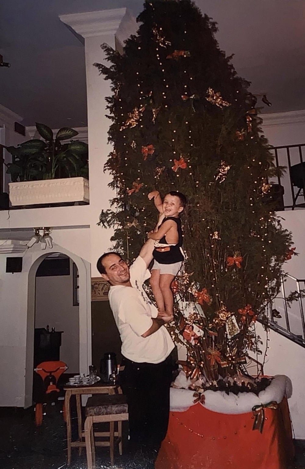 A man lifts a smiling child to reach a decorated Christmas tree.