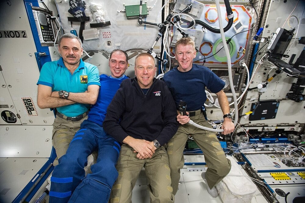 Four astronauts in casual clothing pose together inside the International Space Station.