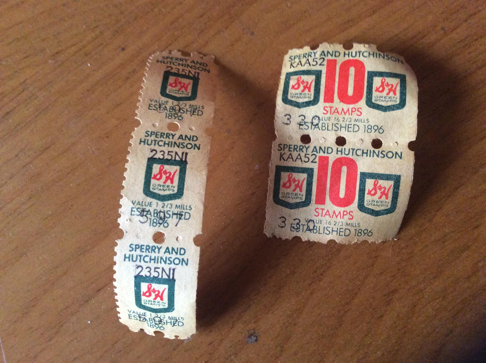 Two strips of vintage Sperry and Hutchinson S&H Green Stamps on a wooden surface, one with single stamps and one with a 10-stamp block, both showing signs of wear and age.