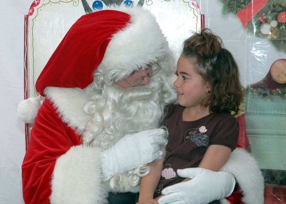 Santa Claus sits with a smiling young girl on his lap.