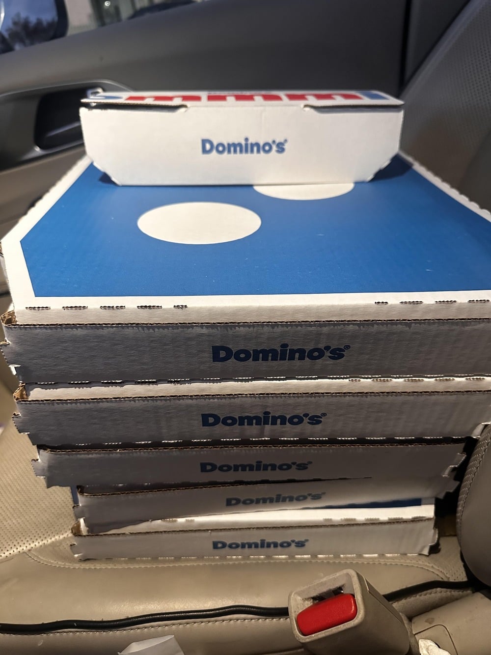 A stack of Domino’s pizza boxes sits on a car seat.