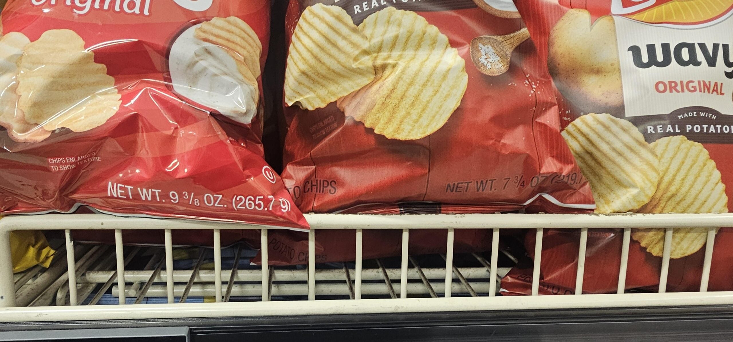 Bags of Lay's Wavy Original potato chips on a grocery store shelf, with red packaging and crinkle-cut chips pictured on the front.
