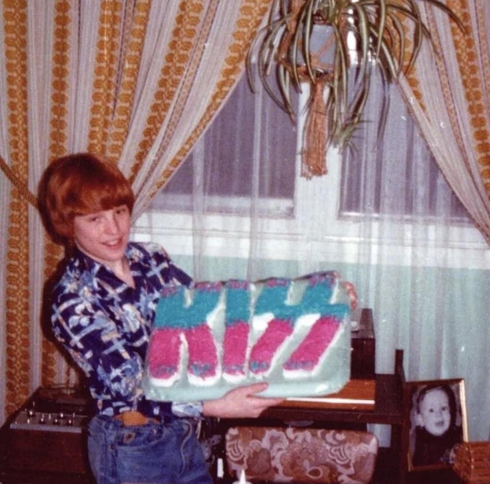 A smiling child holds a large KISS-logo birthday cake.