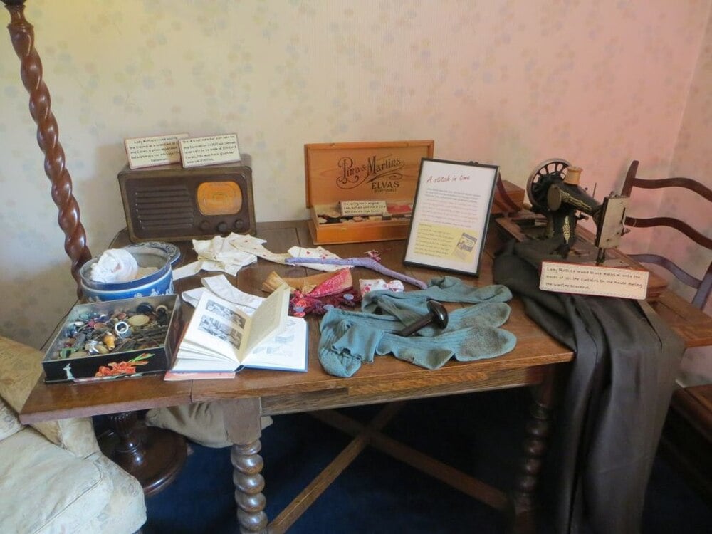 A historic sewing room with a sewing machine, fabric, supplies, and wooden furniture.