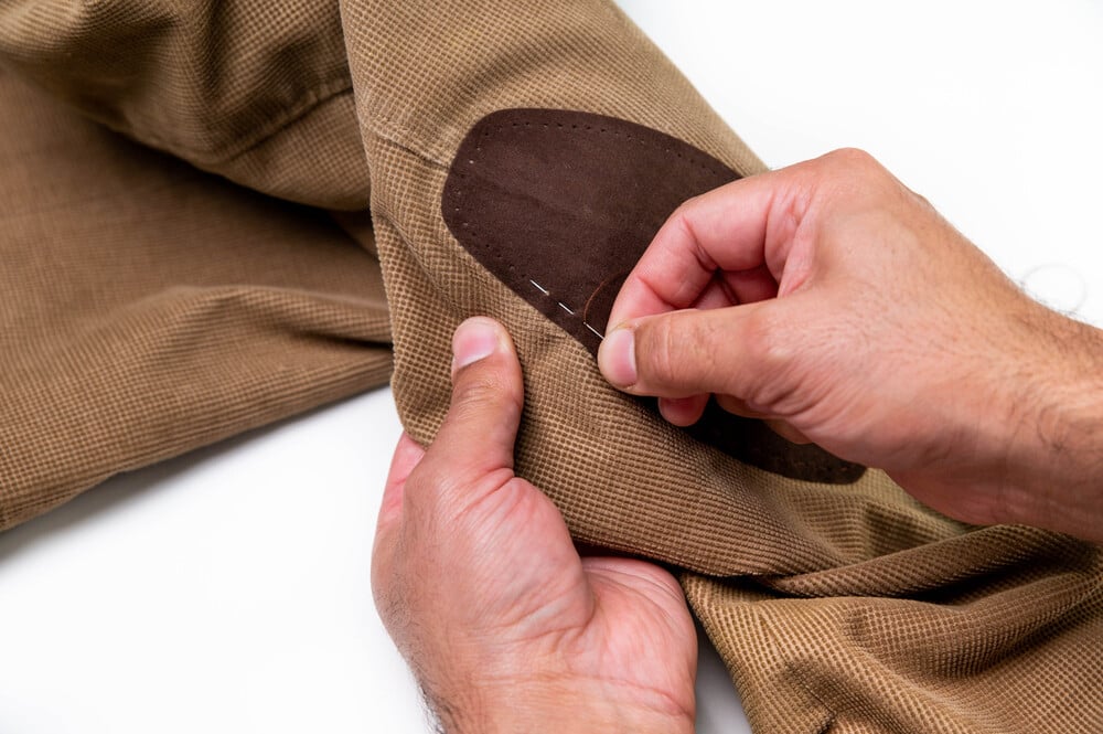A person hand-stitching an elbow patch onto a work shirt.