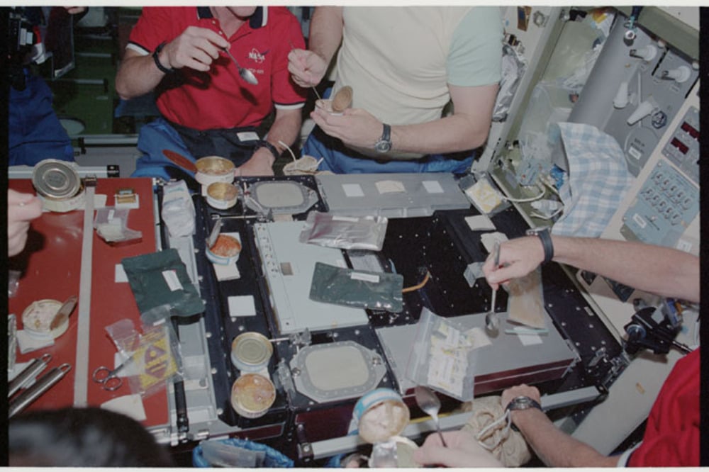 Astronauts share a meal aboard a spacecraft.