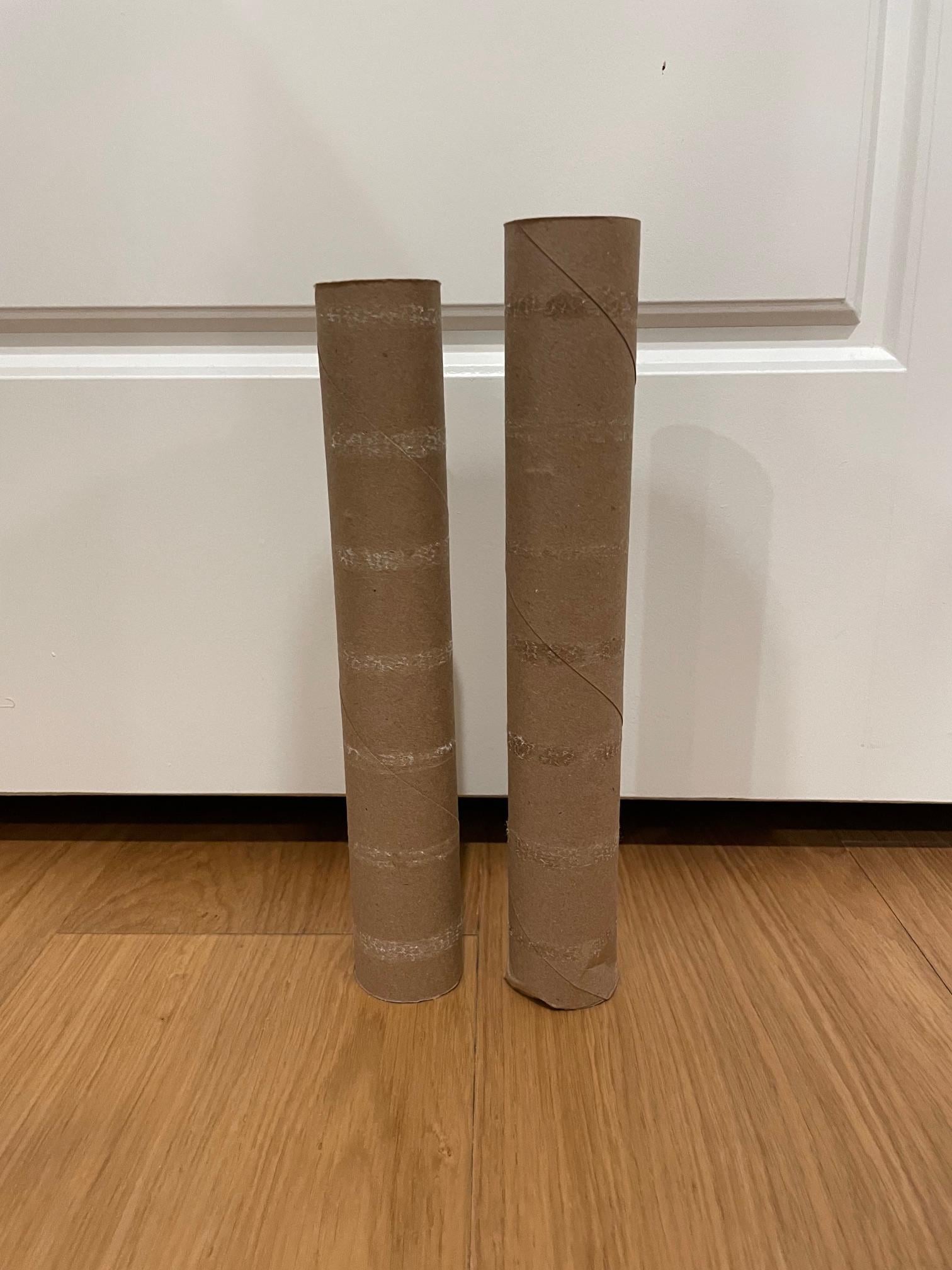 Two empty cardboard paper towel rolls stand upright on a wooden floor.