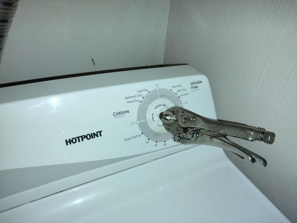 A dryer control panel with locking pliers attached to the main dial, likely used as a handle to turn the setting. The brand “Hotpoint” is visible on the panel.