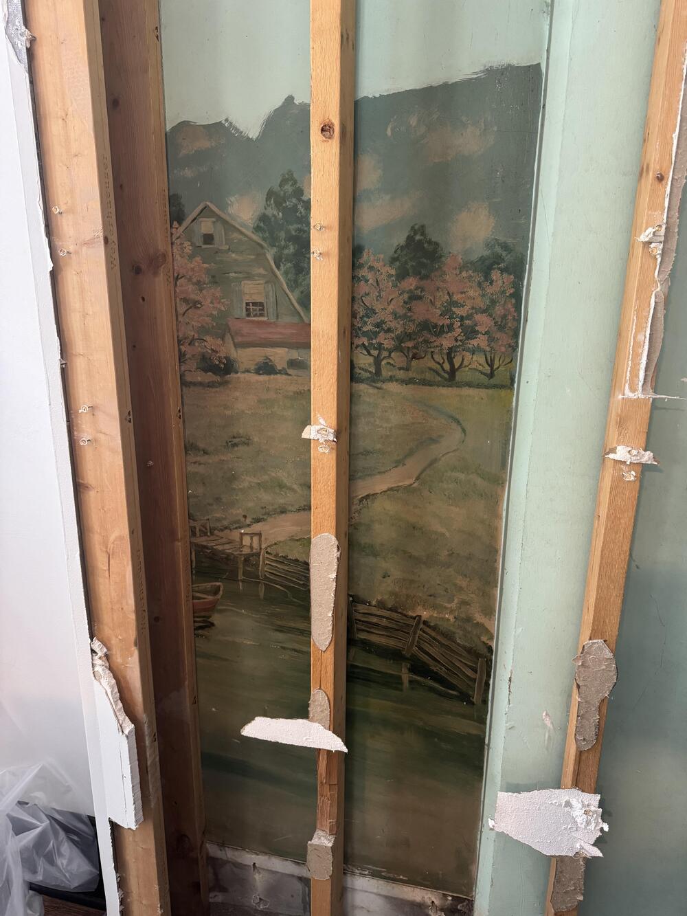 A painted mural partially revealed behind wooden wall studs during renovation.