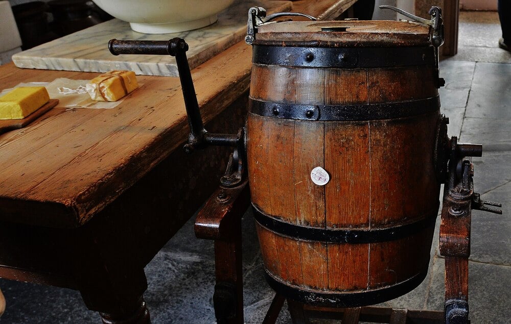 A historic dairy scullery with a wooden butter churn and work table.