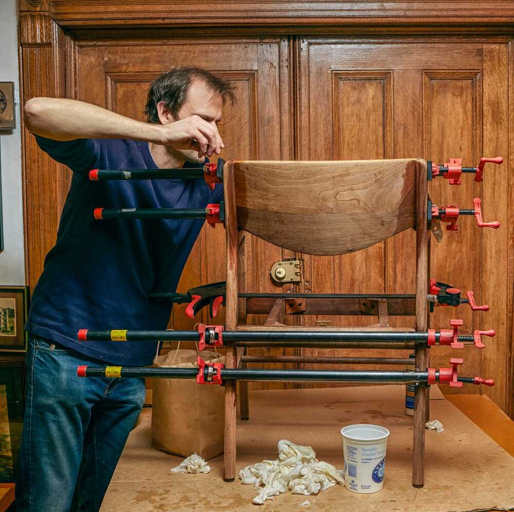 A person using clamps to repair a wooden chair in a workshop.
