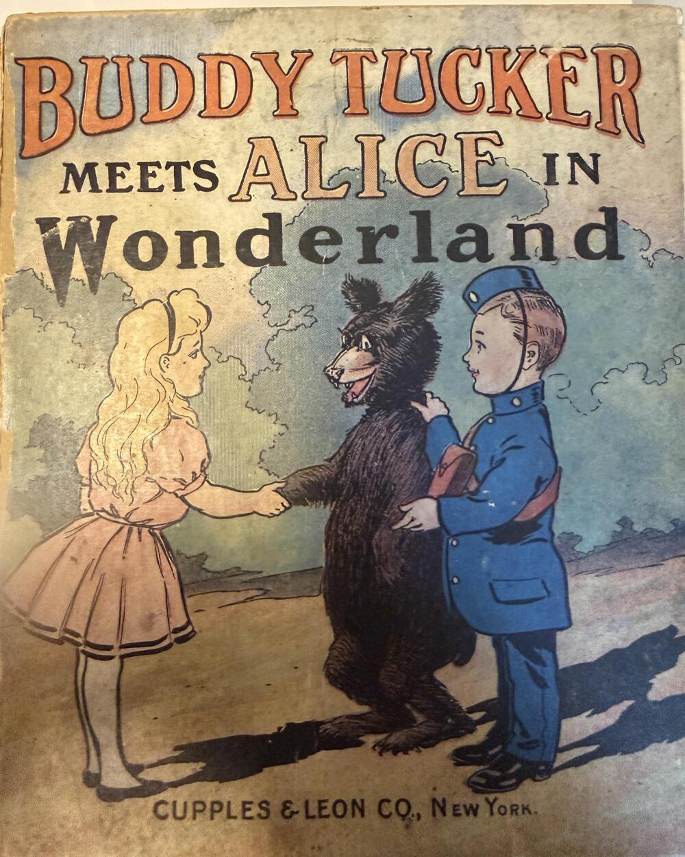 Vintage book cover titled “Buddy Tucker Meets Alice in Wonderland,” showing Alice shaking hands with a boy in blue and a bear standing between them. Published by Cupples & Leon Co., New York.