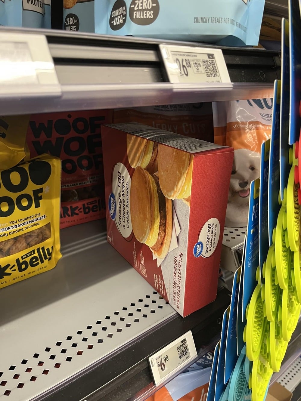 A box of Great Value buttermilk pancakes sits misplaced on a pet food shelf among dog treats and cat food at a grocery store.