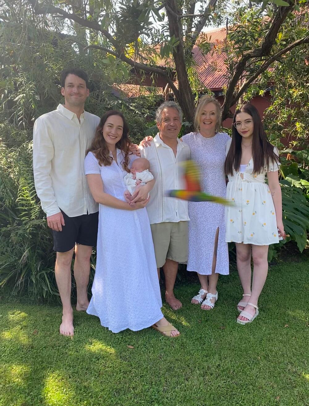 A colorful bird flies directly across a family portrait in a garden.