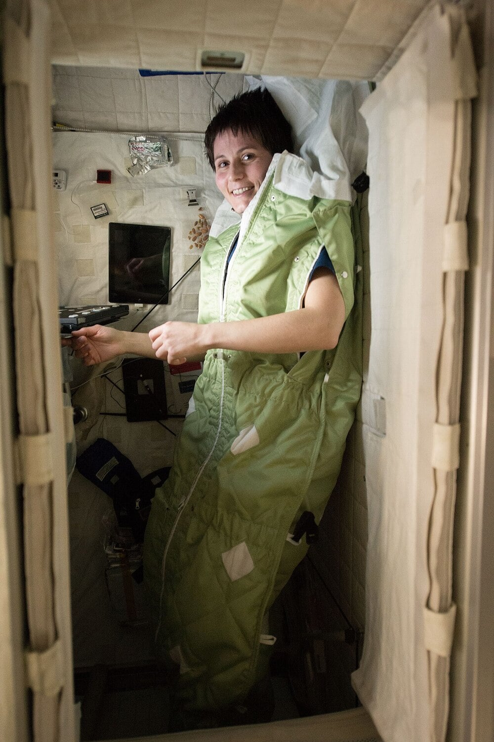 An astronaut rests in a secured sleeping bag inside a space station.