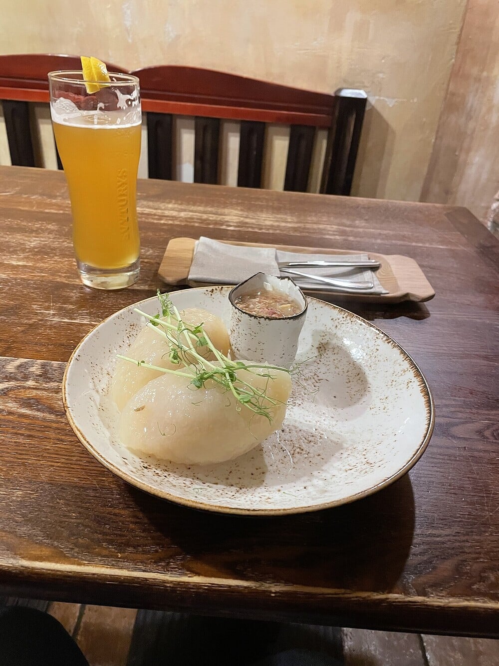 A plate of dumplings sits beside a glass of beer on a wooden table.