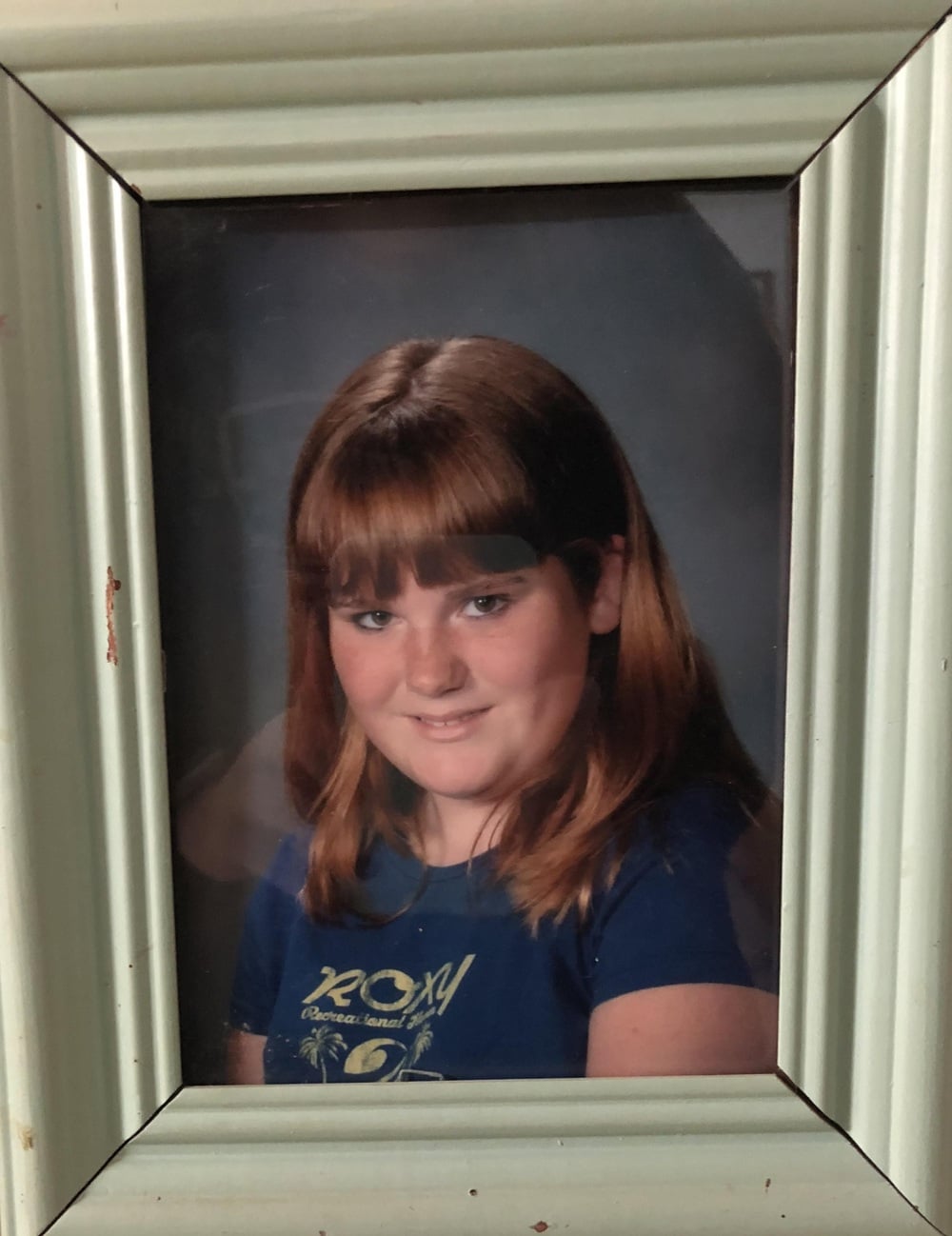 A framed school portrait of a young girl with brown hair and bangs.