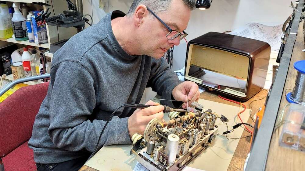 A person repairing vintage radio equipment at a workbench.