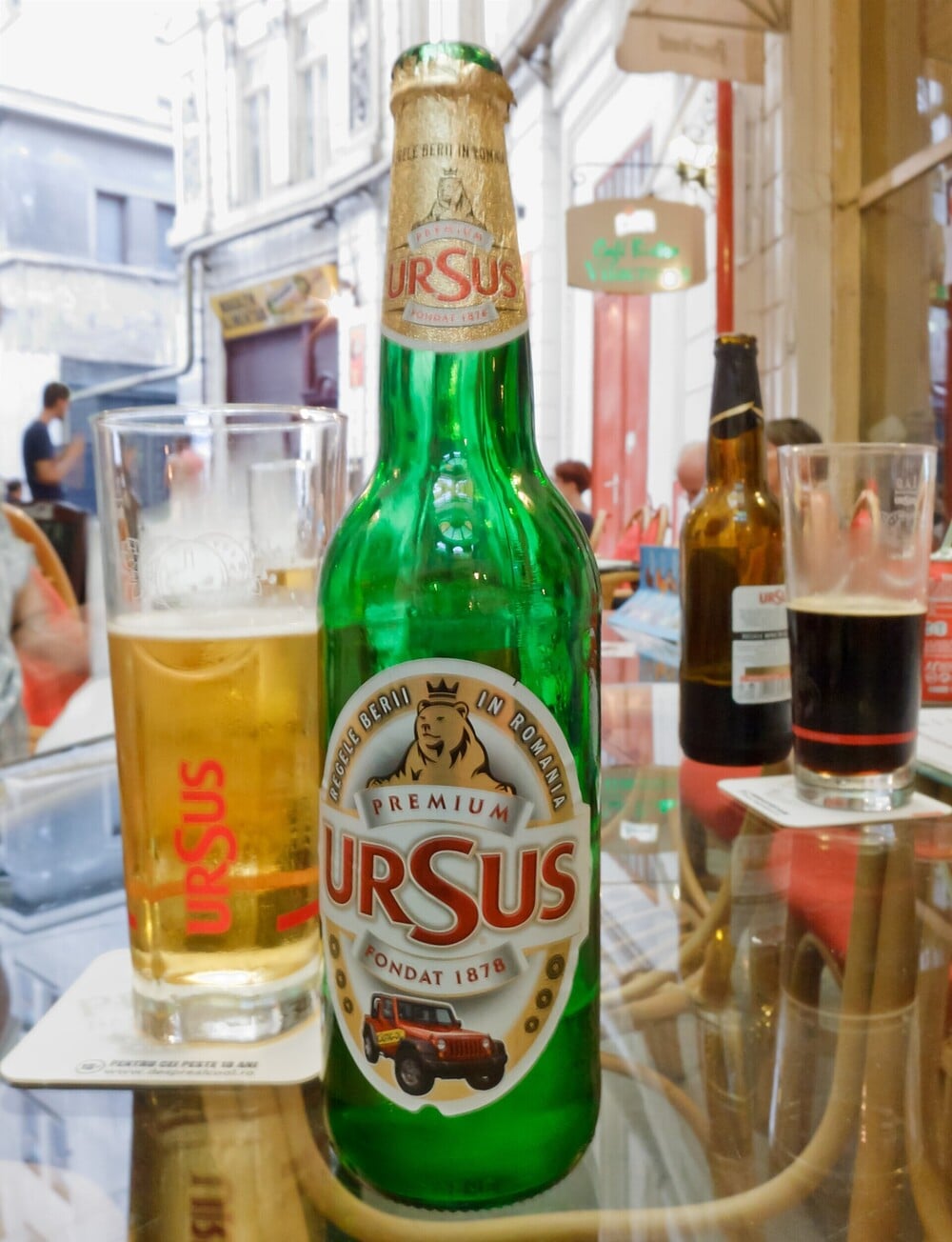 A green beer bottle and a glass of beer on an outdoor cafe table.