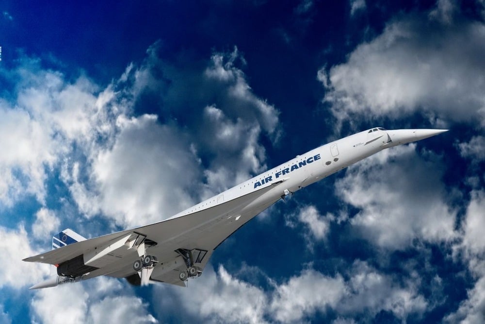 An Air France Concorde jet with a pointed nose ascends into a cloudy blue sky, highlighting its sleek, delta-wing design.