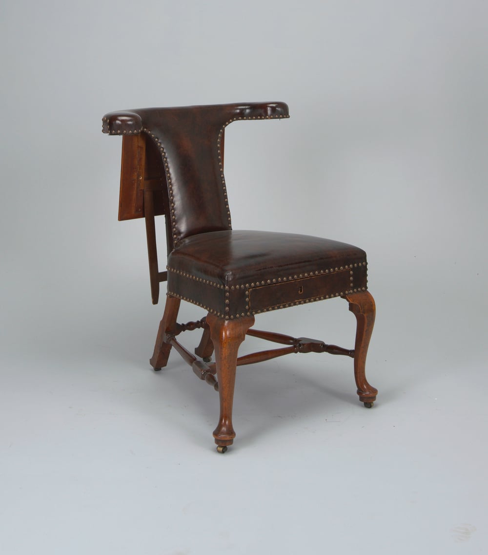 A vintage wooden chair with curved legs and a dark brown leather seat and backrest. The leather is accented with brass studs, and the back curves partially around the sides.