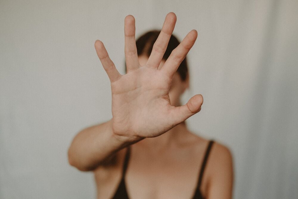 A person holds their hand up toward the camera, palm open, obscuring their face.