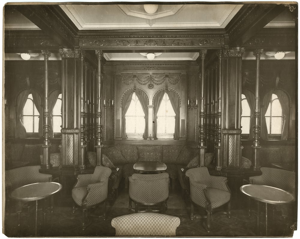 An elegant historic smoking room with wood paneling, arched windows, and upholstered chairs.