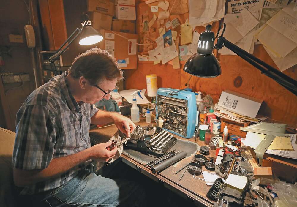 A person repairing a typewriter at a workbench.