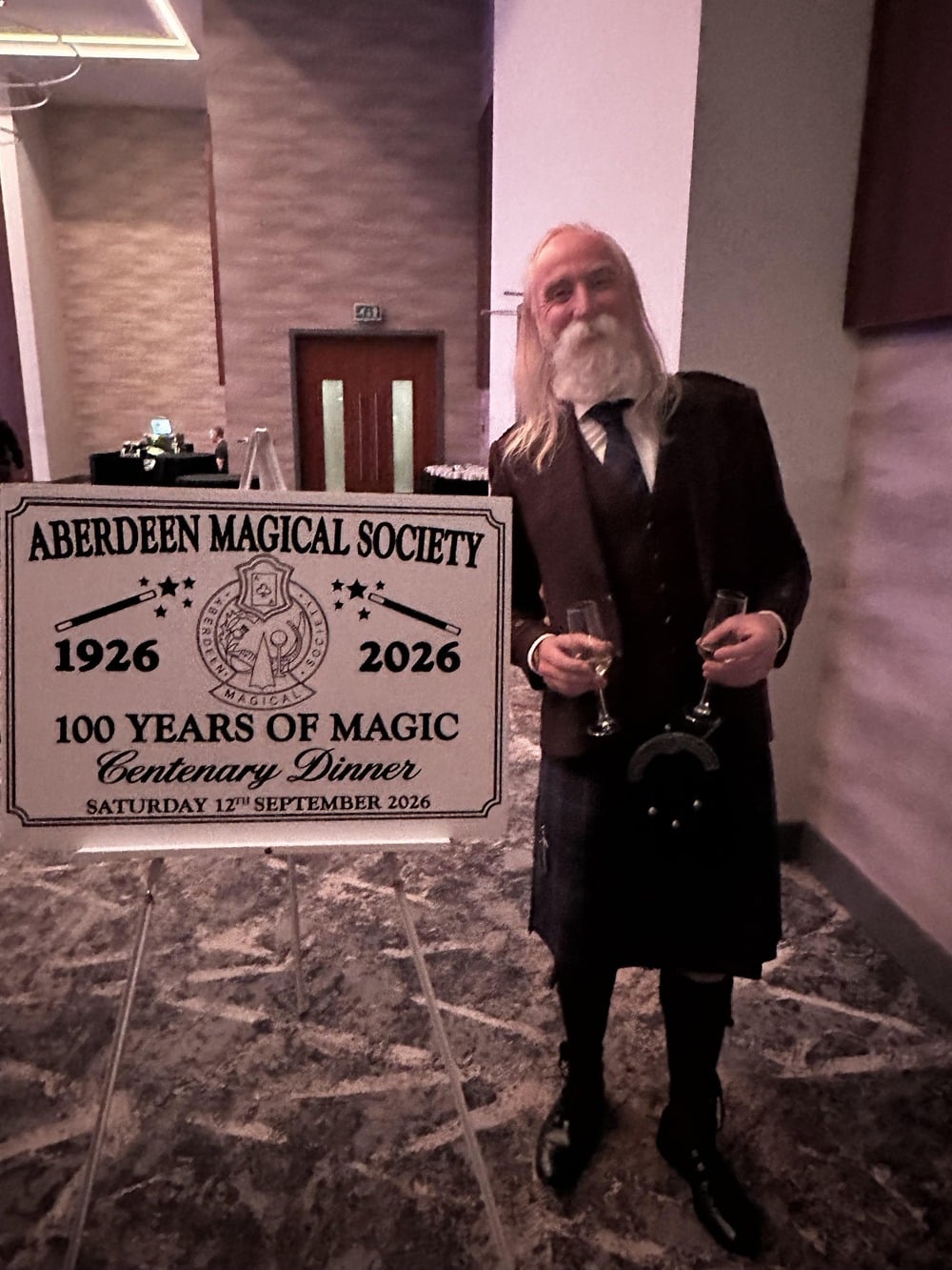 A magician stands beside an Aberdeen Magical Society sign.