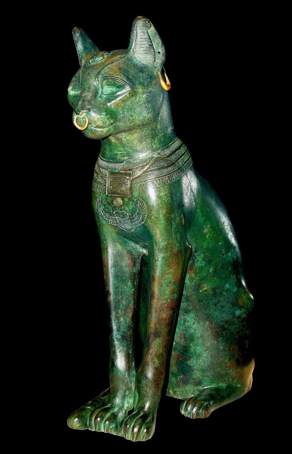 A bronze ancient Egyptian cat statue with gold earrings and a nose ring, adorned with an ornate necklace, sitting upright against a black background.