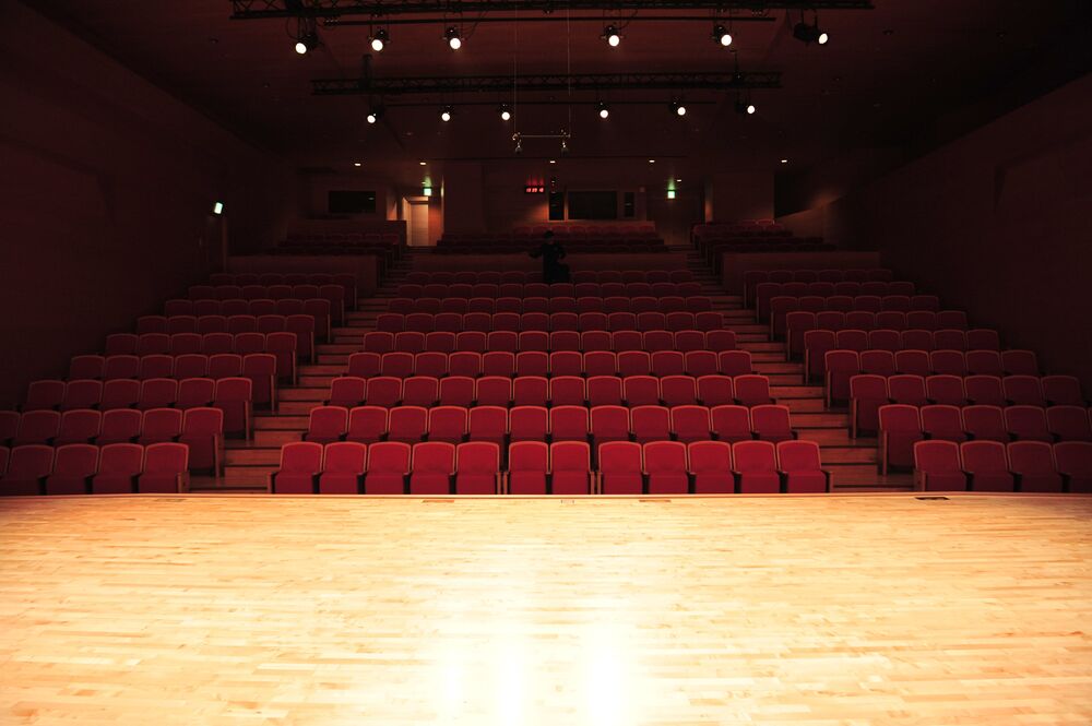 View from a stage looking out at empty red theater seats arranged in rows.